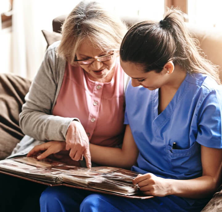 Shot of a nurse and a senior woman looking at a photo album together.
